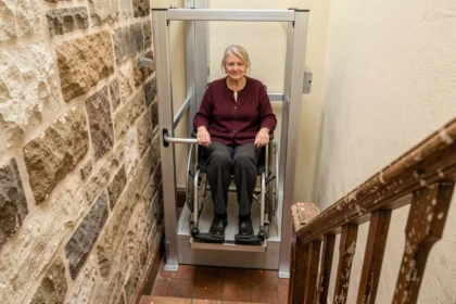 Élévateur PMR vertical installé dans un escalier étroit d'un immeuble ancien en rénovation, avec une femme en fauteuil roulant utilisant la plateforme